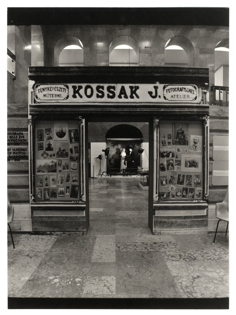 Fényképészkirakat az 1890-es évekből A fotográfia első száz éve Magyarországon című kiállításon. Az installáció Kossak József temesvári fényképész portálja fényképének felhasználásával készült. Farkas Árpád és Jaksity László felvétele, 1987, Legújabb kori Történeti Múzeum